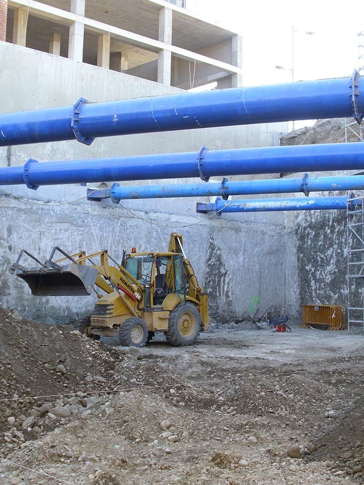 Una excavadora está en medio de un sitio de construcción con tuberías azules.