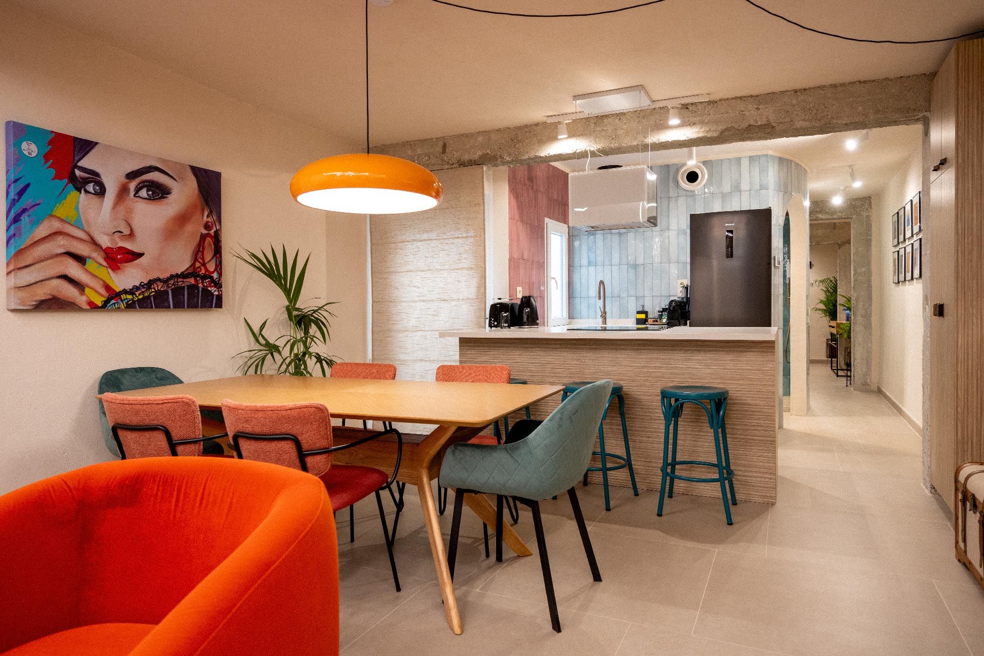 vivienda-calle-peña-proyecto-interiorismo-viviendas-turisticas-blancacano-d-21 Un comedor contemporáneo con sillas coloridas, una gran lámpara colgante, una obra de arte enmarcada en la pared y una cocina moderna contigua al fondo.