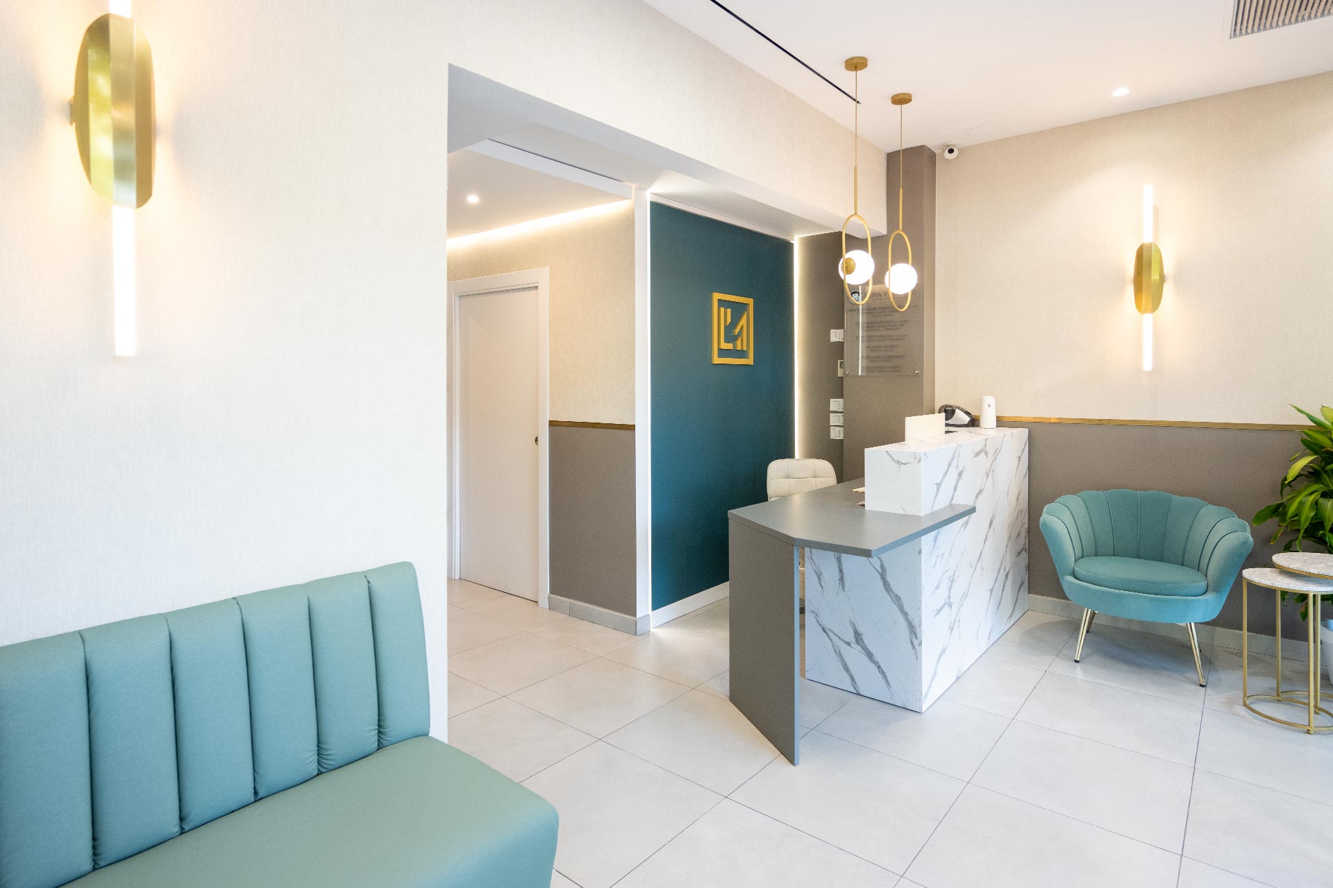 Recepción de oficina moderna con mostrador de mármol, asientos color verde azulado, luces colgantes y decoración minimalista.