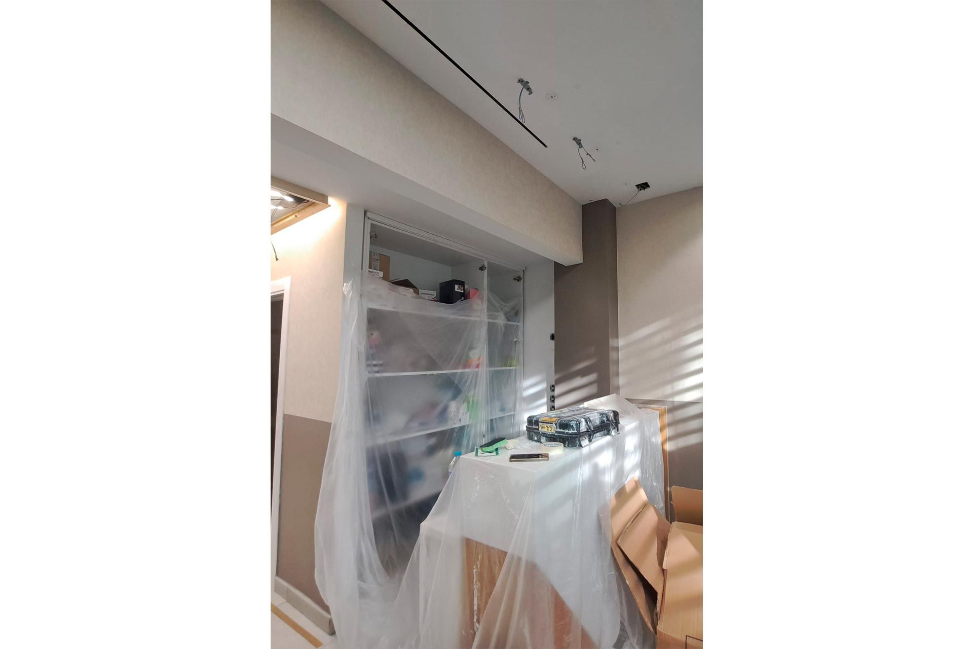 Habitación en reforma con muebles forrados, estanterías expuestas y cableado del techo visible.