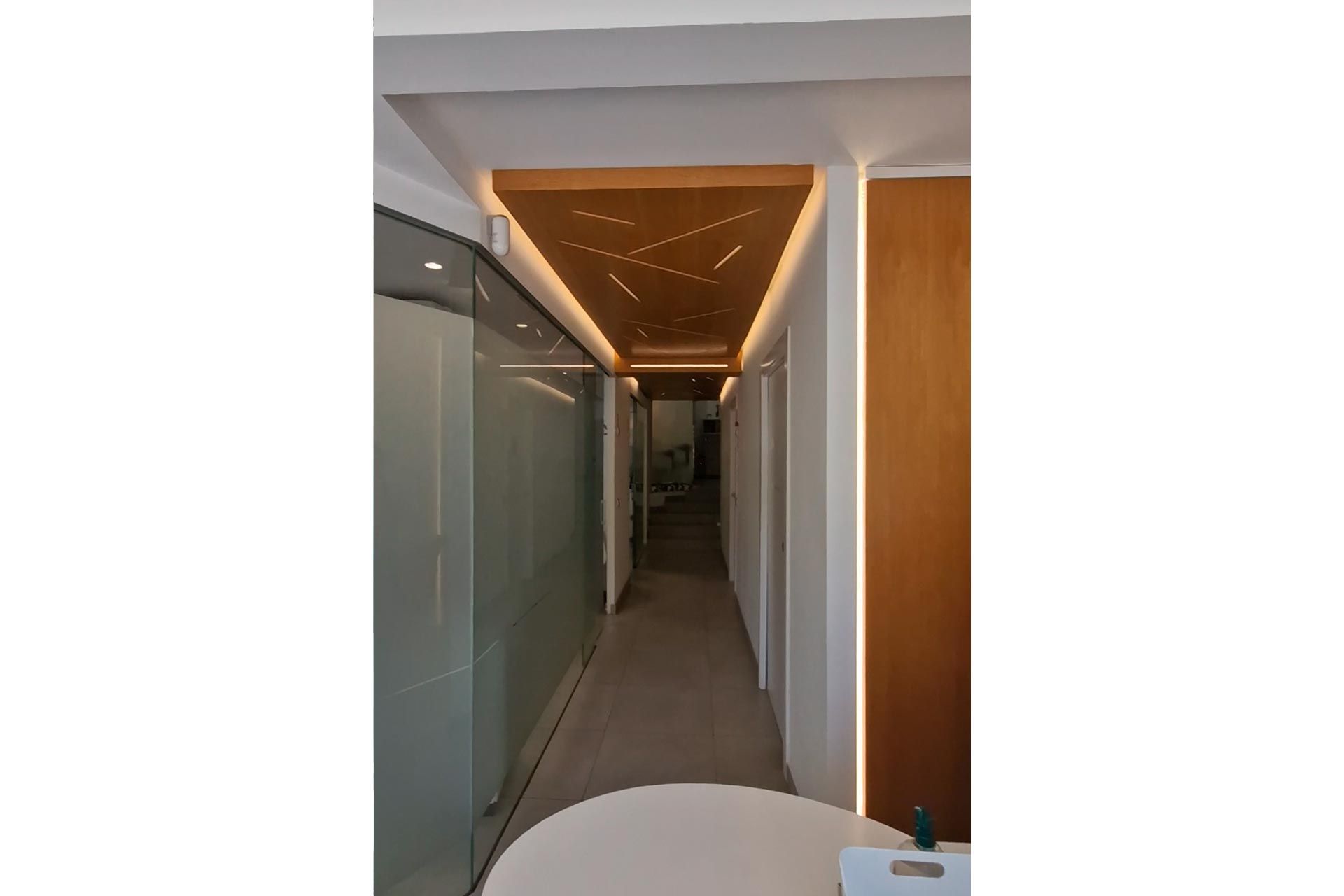 Un pasillo moderno con paredes de vidrio esmerilado y un techo de madera con patrones de luz geométricos.