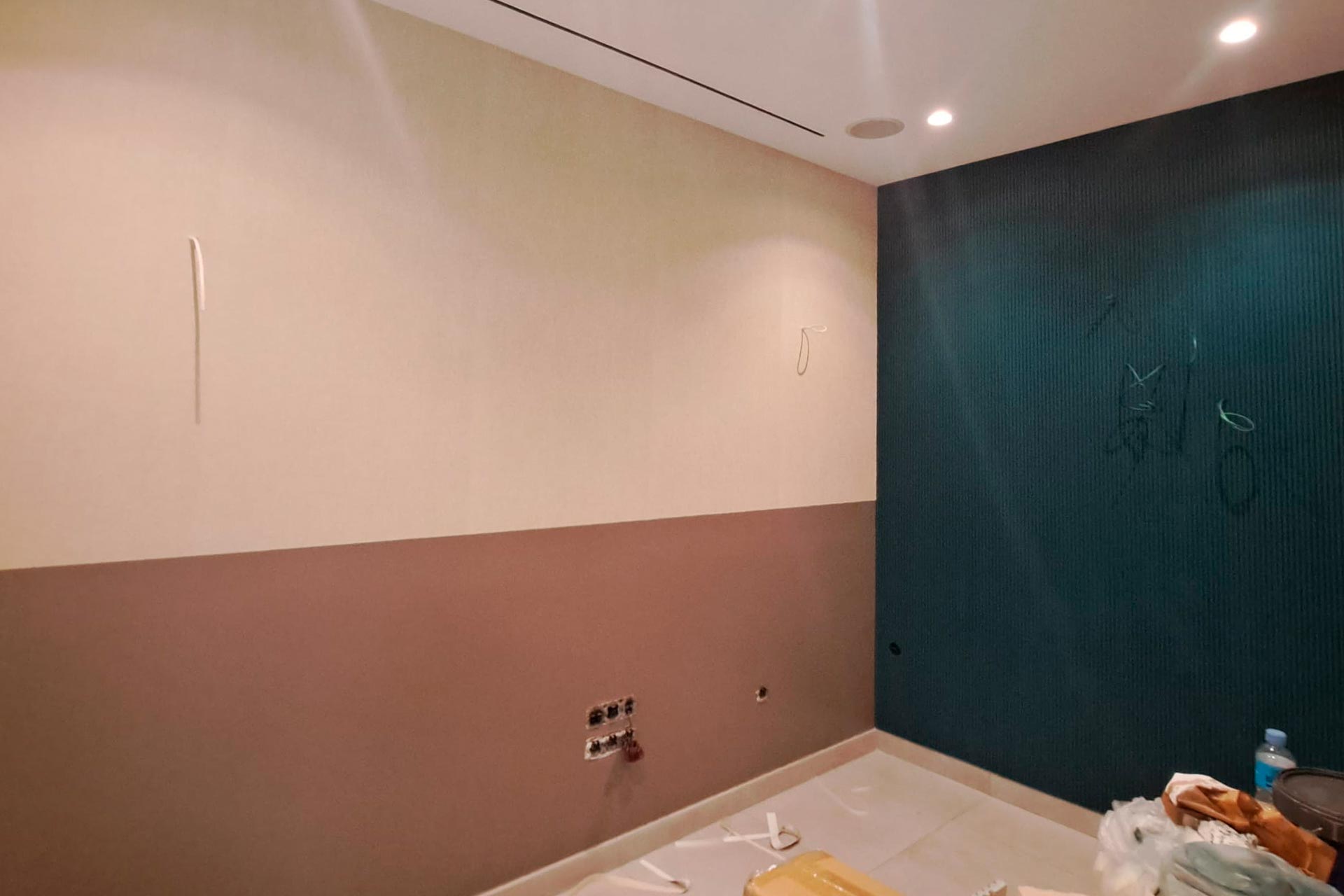 Una habitación parcialmente construida con paredes de color beige, marrón y verde azulado. Se ven cables y enchufes eléctricos. Hay materiales de construcción esparcidos por el suelo.