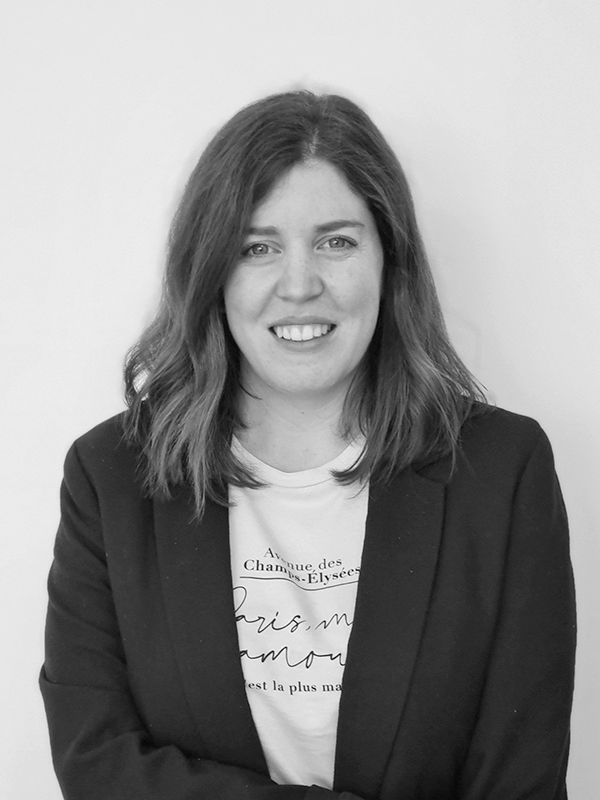 Natalia-Gil Mujer con cabello hasta los hombros, con un blazer sobre una camisa estampada, sonriendo en un retrato en blanco y negro.