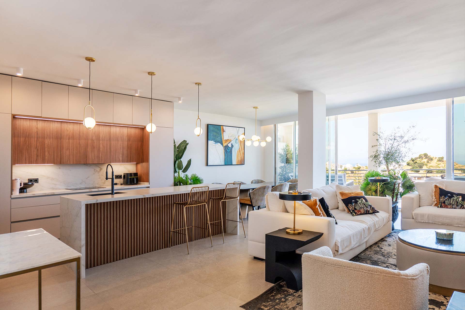 Interiorismo-Atico-Benalmadena-BlancaCano-Salon-009 Moderna cocina y sala de estar de planta abierta con tonos neutros, lámparas colgantes, una isla de mármol y grandes ventanales que dejan entrar la luz natural.