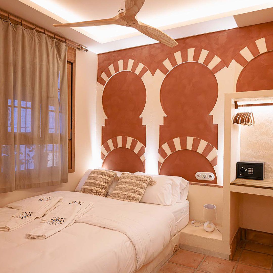 Una moderna sala de estar y comedor con un sofá redondo turquesa con cojines amarillos, una cómoda de madera, un televisor montado en la pared, plantas en macetas y una mesa de comedor con cuatro sillas marrones.
